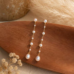 Long gold-tone drop earrings featuring natural freshwater pearls; minimalist-style 18K gold-plated earrings