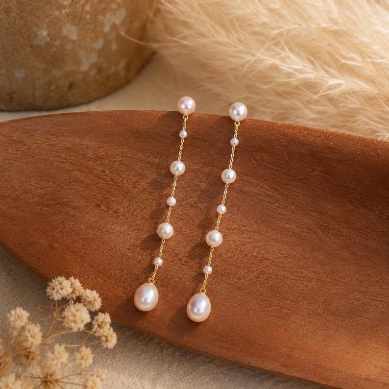 Long gold-tone drop earrings featuring natural freshwater pearls; minimalist-style 18K gold-plated earrings