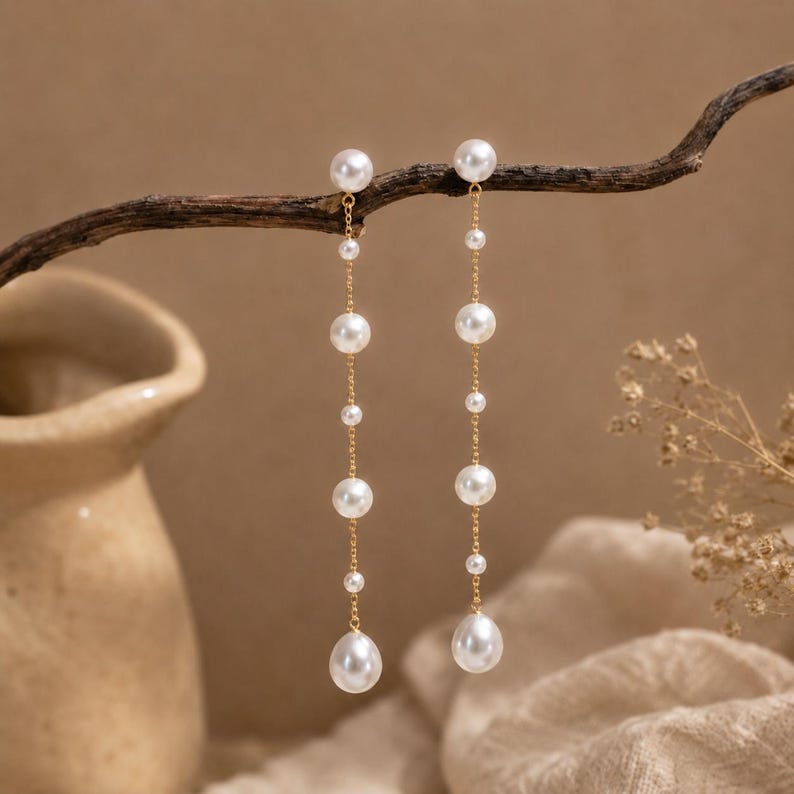 Long gold-tone drop earrings featuring natural freshwater pearls; minimalist-style 18K gold-plated earrings