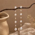 Long gold-tone drop earrings featuring natural freshwater pearls; minimalist-style 18K gold-plated earrings
