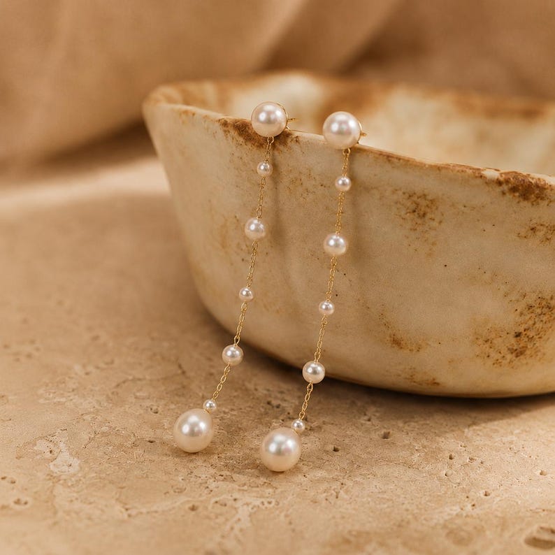 Long gold-tone drop earrings featuring natural freshwater pearls; minimalist-style 18K gold-plated earrings